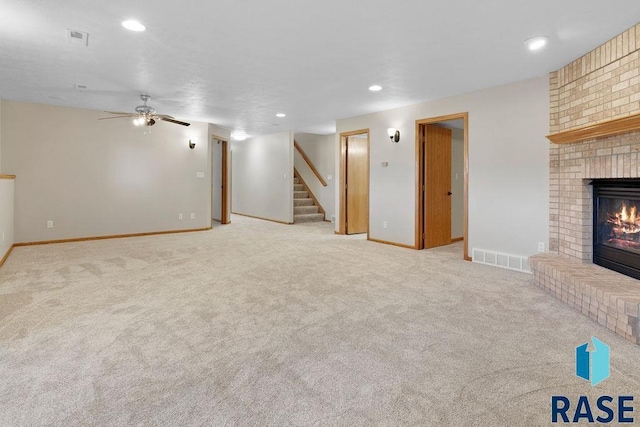 unfurnished living room featuring ceiling fan, light colored carpet, and a brick fireplace