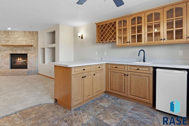 kitchen featuring sink, ceiling fan, white dishwasher, a brick fireplace, and kitchen peninsula