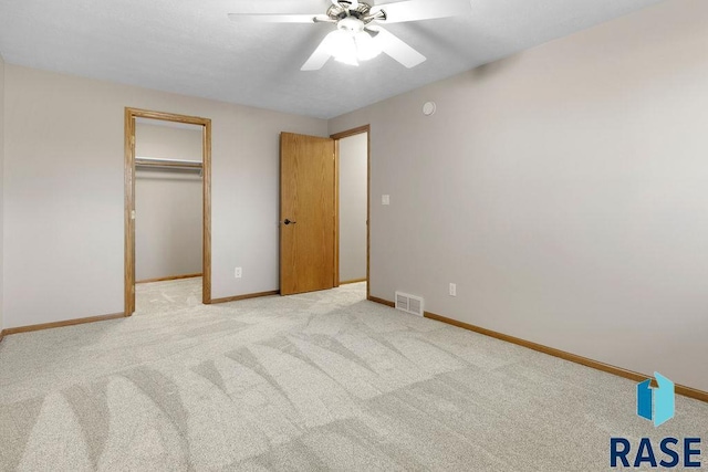 unfurnished bedroom with ceiling fan, a spacious closet, a closet, and light carpet