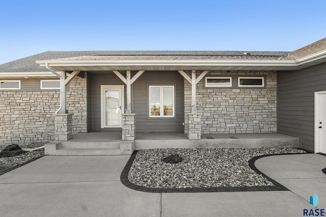 property entrance with stone siding, a porch, and a shingled roof