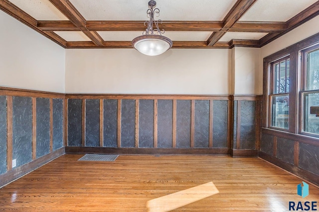 empty room featuring beamed ceiling, coffered ceiling, and light hardwood / wood-style flooring