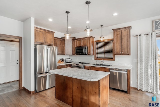 kitchen featuring sink, decorative light fixtures, appliances with stainless steel finishes, a kitchen island, and light hardwood / wood-style floors