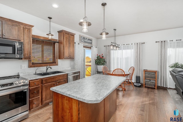 kitchen with pendant lighting, sink, a center island, stainless steel appliances, and light wood-type flooring