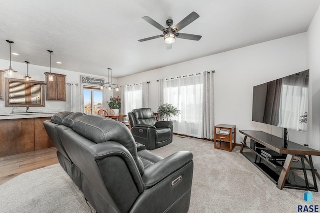 living room with sink, ceiling fan with notable chandelier, and light wood-type flooring