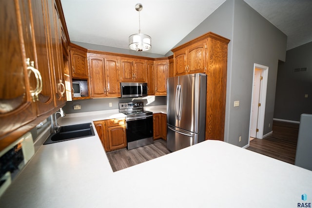 kitchen featuring sink, vaulted ceiling, appliances with stainless steel finishes, dark hardwood / wood-style floors, and pendant lighting