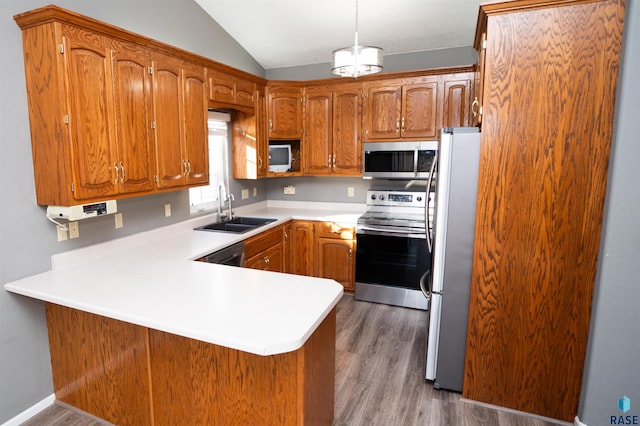 kitchen with sink, appliances with stainless steel finishes, kitchen peninsula, pendant lighting, and light hardwood / wood-style floors