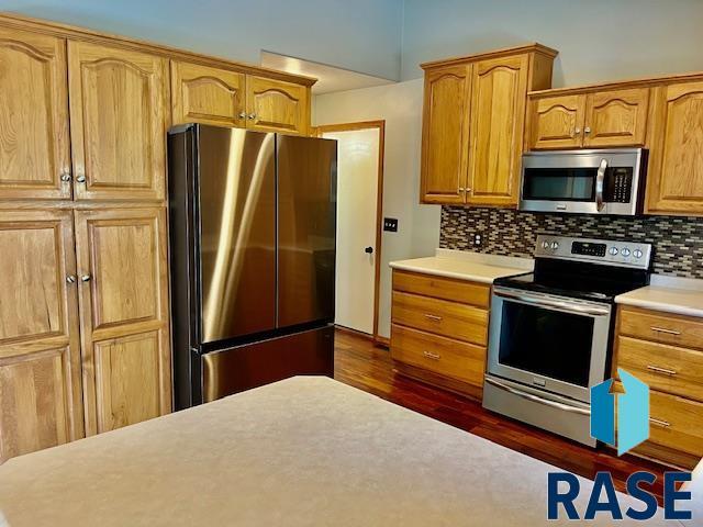 kitchen with stainless steel appliances, dark wood-type flooring, and backsplash