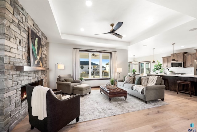 living room featuring a fireplace, sink, ceiling fan, a raised ceiling, and light hardwood / wood-style flooring