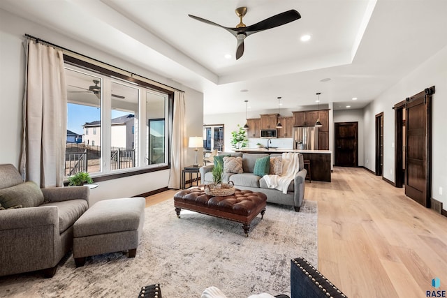 living room with ceiling fan, light hardwood / wood-style flooring, a barn door, and a raised ceiling