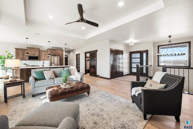 living room with sink, ceiling fan, a tray ceiling, light hardwood / wood-style floors, and a barn door