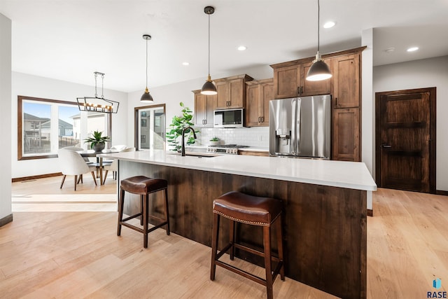 kitchen with tasteful backsplash, decorative light fixtures, light hardwood / wood-style flooring, and appliances with stainless steel finishes