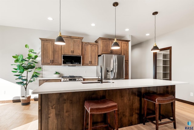 kitchen with pendant lighting, stainless steel appliances, a kitchen island with sink, and decorative backsplash