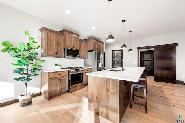 kitchen featuring sink, a center island with sink, appliances with stainless steel finishes, pendant lighting, and decorative backsplash