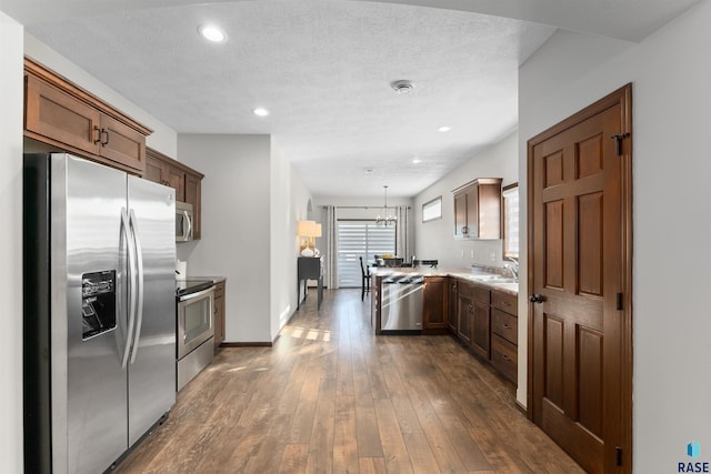 kitchen with sink, dark wood-type flooring, appliances with stainless steel finishes, a textured ceiling, and decorative light fixtures