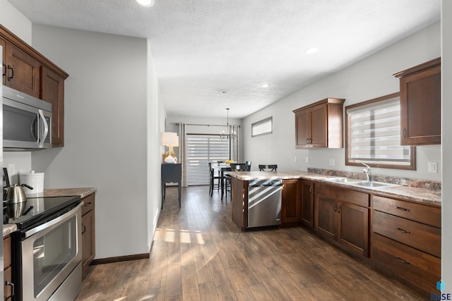 kitchen featuring sink, decorative light fixtures, appliances with stainless steel finishes, dark hardwood / wood-style flooring, and kitchen peninsula