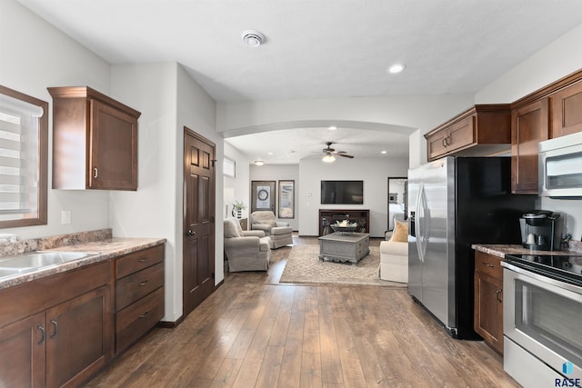 kitchen featuring dark wood-type flooring, sink, light stone counters, ceiling fan, and stainless steel appliances