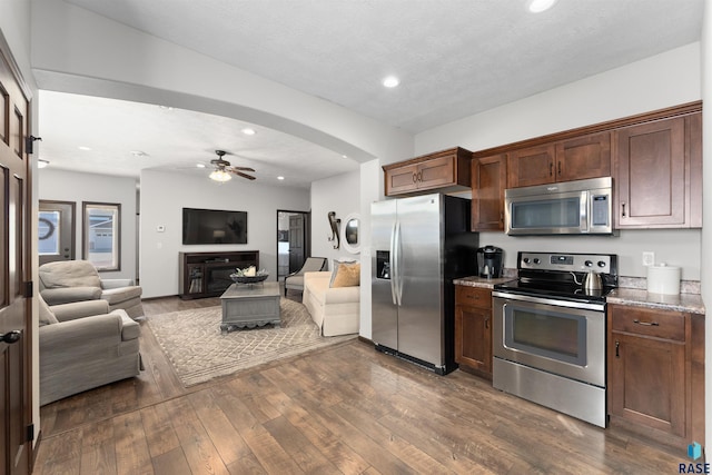 kitchen with stainless steel appliances, ceiling fan, light stone countertops, and dark hardwood / wood-style flooring