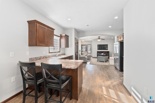 kitchen with stainless steel fridge, ceiling fan, a kitchen breakfast bar, light hardwood / wood-style floors, and kitchen peninsula