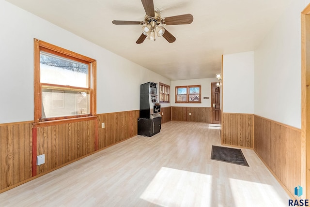 unfurnished living room with ceiling fan, plenty of natural light, wooden walls, and light hardwood / wood-style flooring