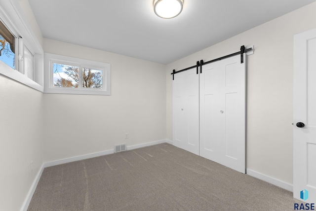 unfurnished bedroom with a barn door, carpet flooring, and a closet