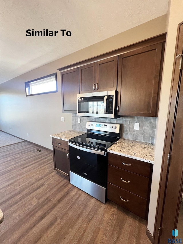 kitchen with dark wood-type flooring, dark brown cabinetry, light stone counters, stainless steel appliances, and backsplash