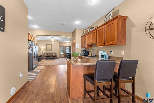 kitchen featuring stone countertops, kitchen peninsula, a kitchen bar, stainless steel fridge with ice dispenser, and light wood-type flooring