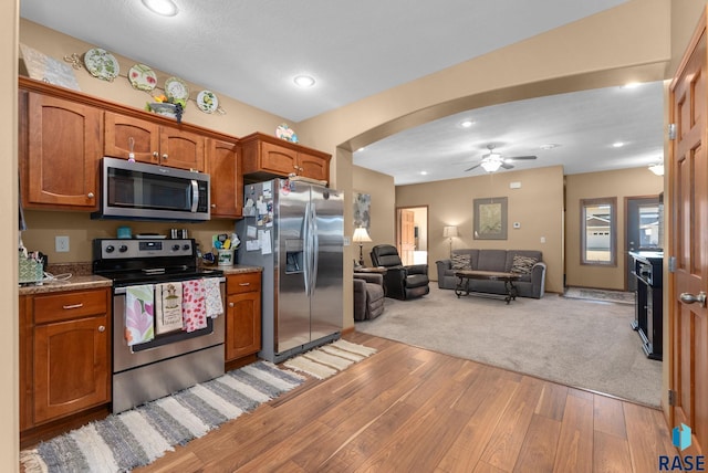 kitchen with stainless steel appliances, ceiling fan, light hardwood / wood-style floors, and dark stone counters