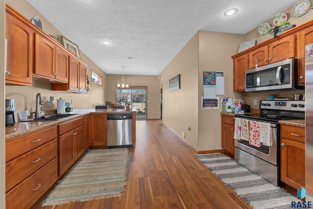 kitchen with pendant lighting, sink, appliances with stainless steel finishes, a notable chandelier, and wood-type flooring