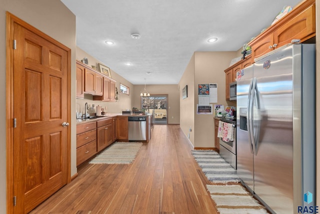 kitchen featuring sink, hanging light fixtures, light hardwood / wood-style floors, stainless steel appliances, and an inviting chandelier