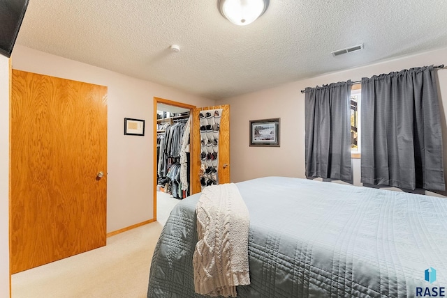 bedroom featuring a spacious closet, light colored carpet, a textured ceiling, and a closet