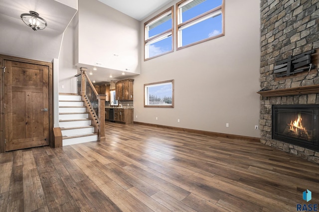 unfurnished living room with dark hardwood / wood-style flooring, a stone fireplace, and a towering ceiling