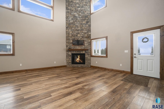 unfurnished living room with a stone fireplace, wood-type flooring, a healthy amount of sunlight, and a high ceiling