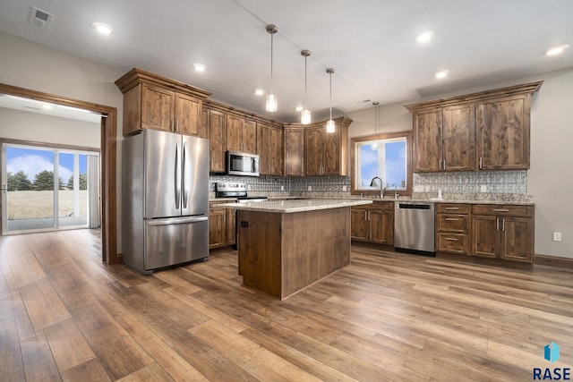 kitchen with wood-type flooring, a center island, hanging light fixtures, stainless steel appliances, and light stone countertops