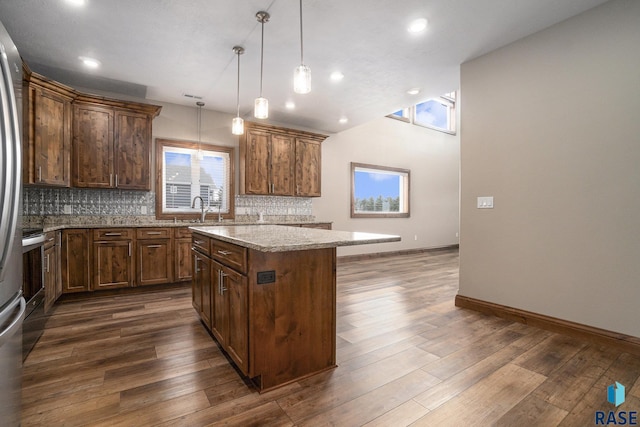 kitchen with tasteful backsplash, a center island, hanging light fixtures, dark hardwood / wood-style flooring, and light stone countertops