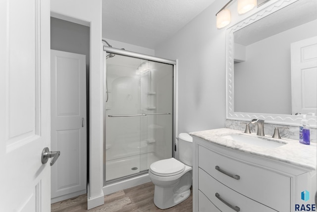 bathroom featuring hardwood / wood-style floors, vanity, walk in shower, toilet, and a textured ceiling