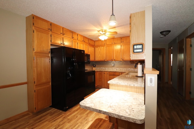 kitchen featuring sink, hanging light fixtures, black appliances, a textured ceiling, and light hardwood / wood-style flooring