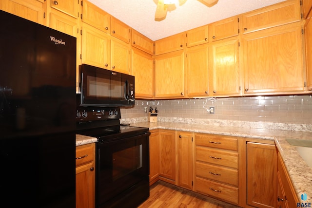 kitchen featuring light stone counters, decorative backsplash, light hardwood / wood-style flooring, and black appliances