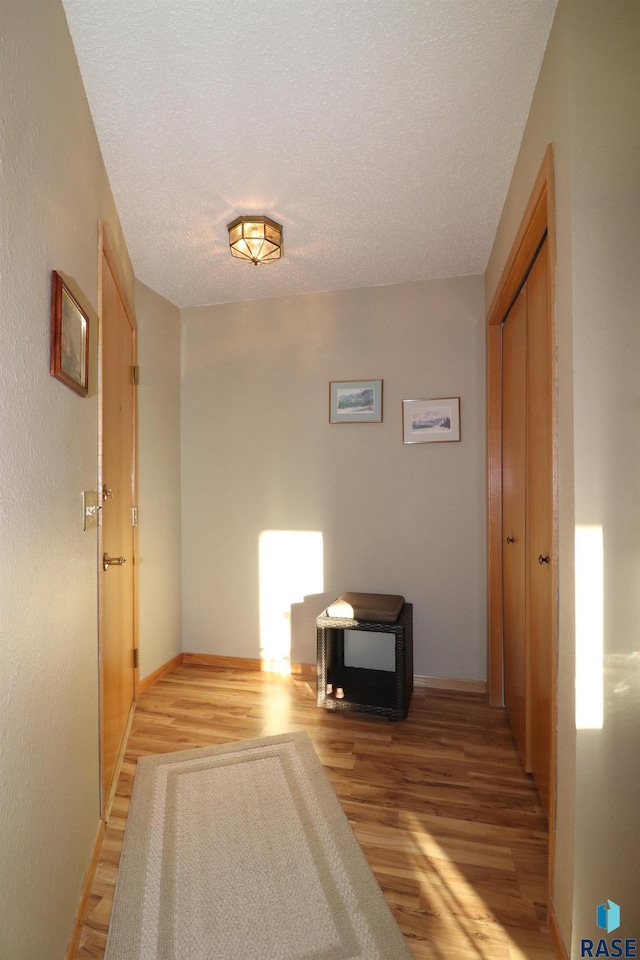 hall with a textured ceiling and light hardwood / wood-style flooring