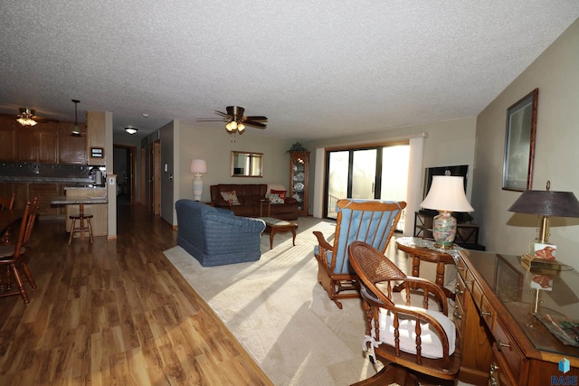 living room featuring a textured ceiling, wood-type flooring, and ceiling fan