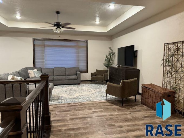 living room with ceiling fan, a raised ceiling, and hardwood / wood-style floors