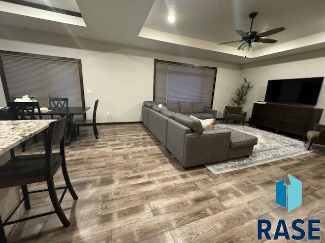 living room with hardwood / wood-style flooring, ceiling fan, and a raised ceiling