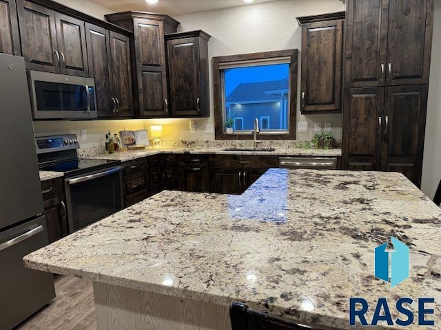 kitchen featuring dark brown cabinetry, appliances with stainless steel finishes, light stone countertops, and sink