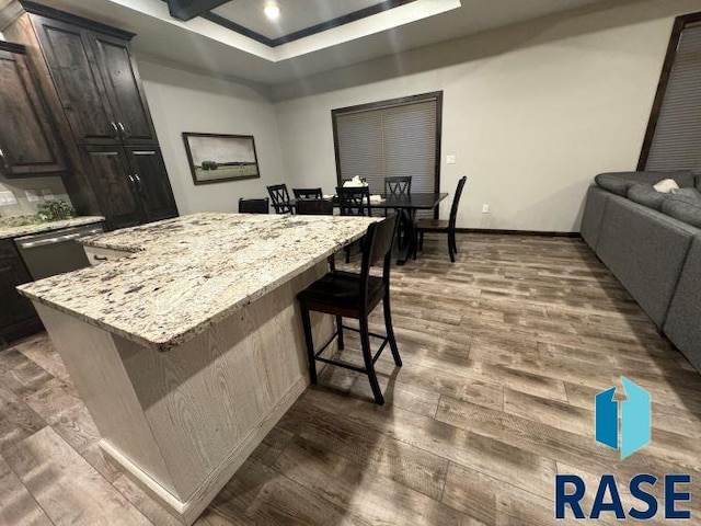 kitchen with dark hardwood / wood-style floors, a kitchen bar, a center island, light stone counters, and dark brown cabinetry