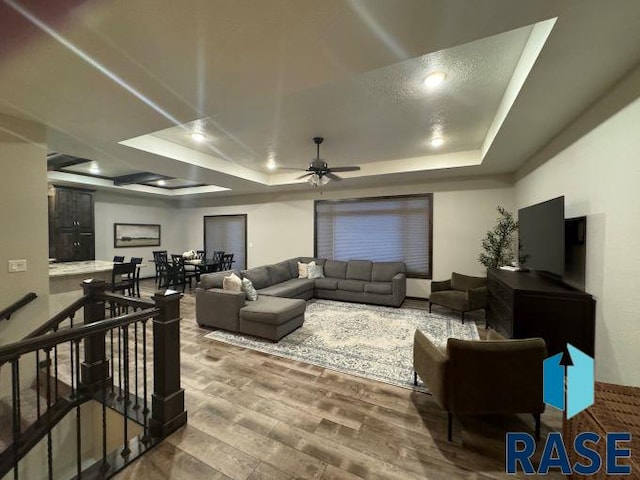 living room featuring ceiling fan, a raised ceiling, and hardwood / wood-style floors