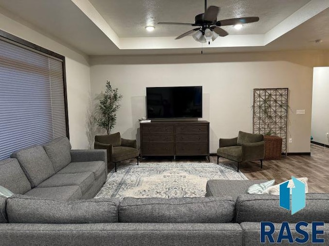 living room with a raised ceiling, wood-type flooring, and ceiling fan