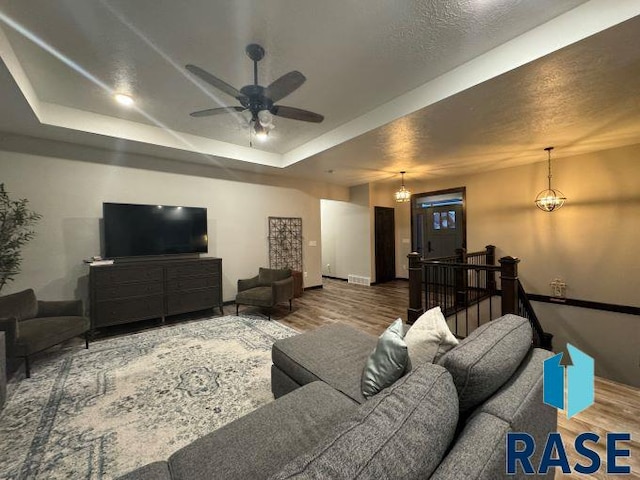 living room featuring a tray ceiling, wood-type flooring, and ceiling fan with notable chandelier