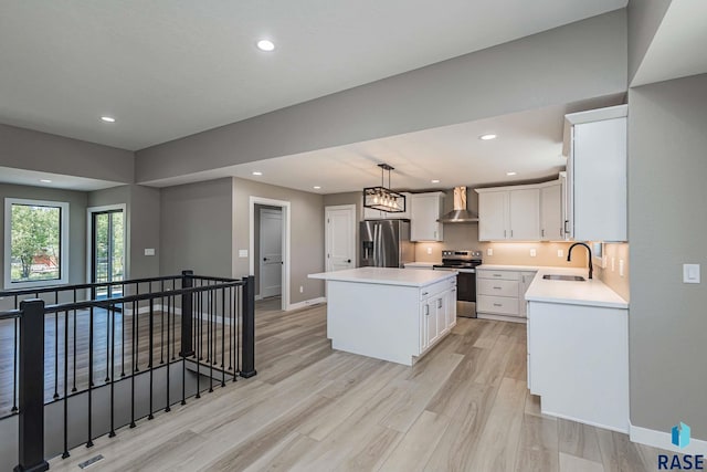 kitchen featuring pendant lighting, wall chimney range hood, appliances with stainless steel finishes, white cabinets, and a kitchen island