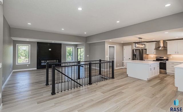 kitchen with stainless steel appliances, a kitchen island, wall chimney range hood, and white cabinets