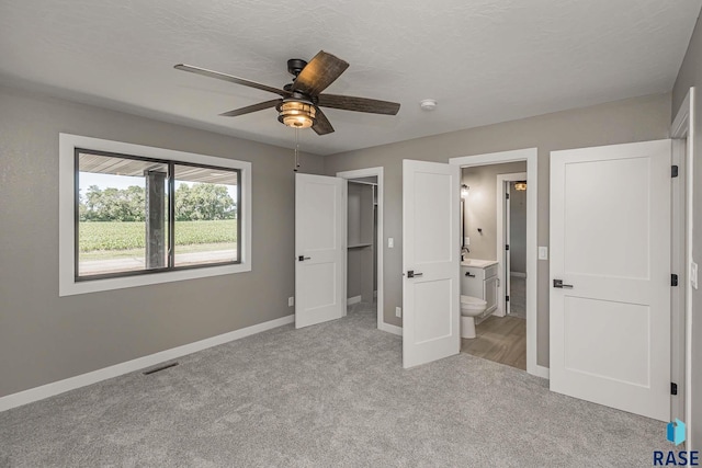 unfurnished bedroom with ceiling fan, light colored carpet, ensuite bathroom, and a textured ceiling