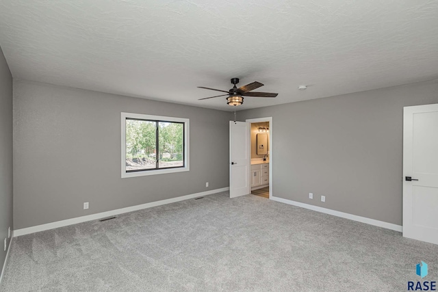 unfurnished bedroom featuring connected bathroom, light carpet, and a textured ceiling